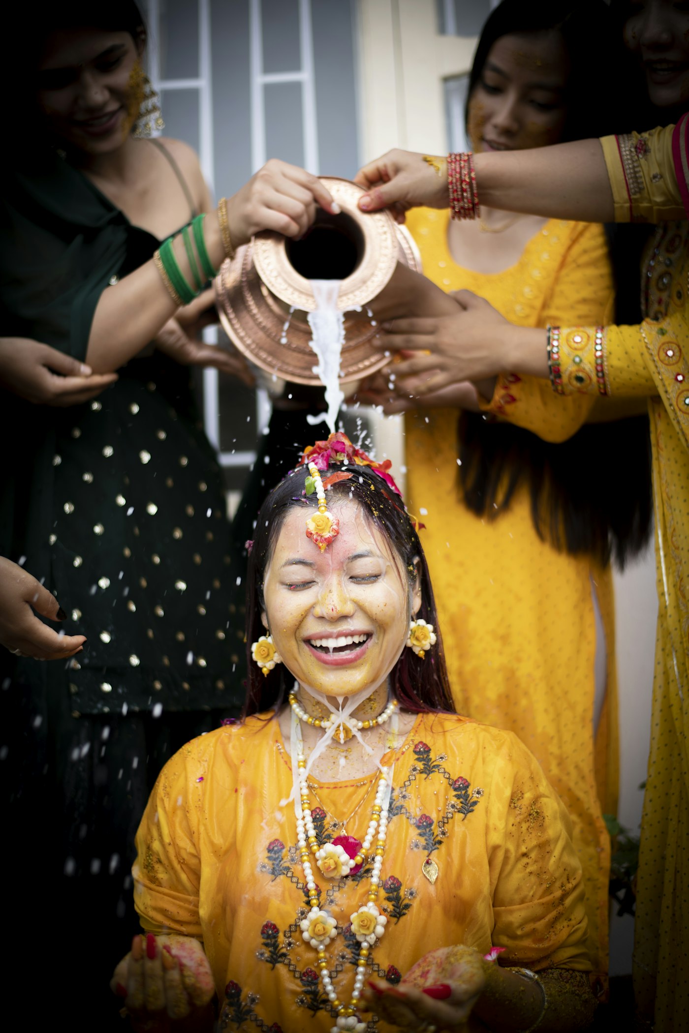 Laughing bride as family pour water at her haldi