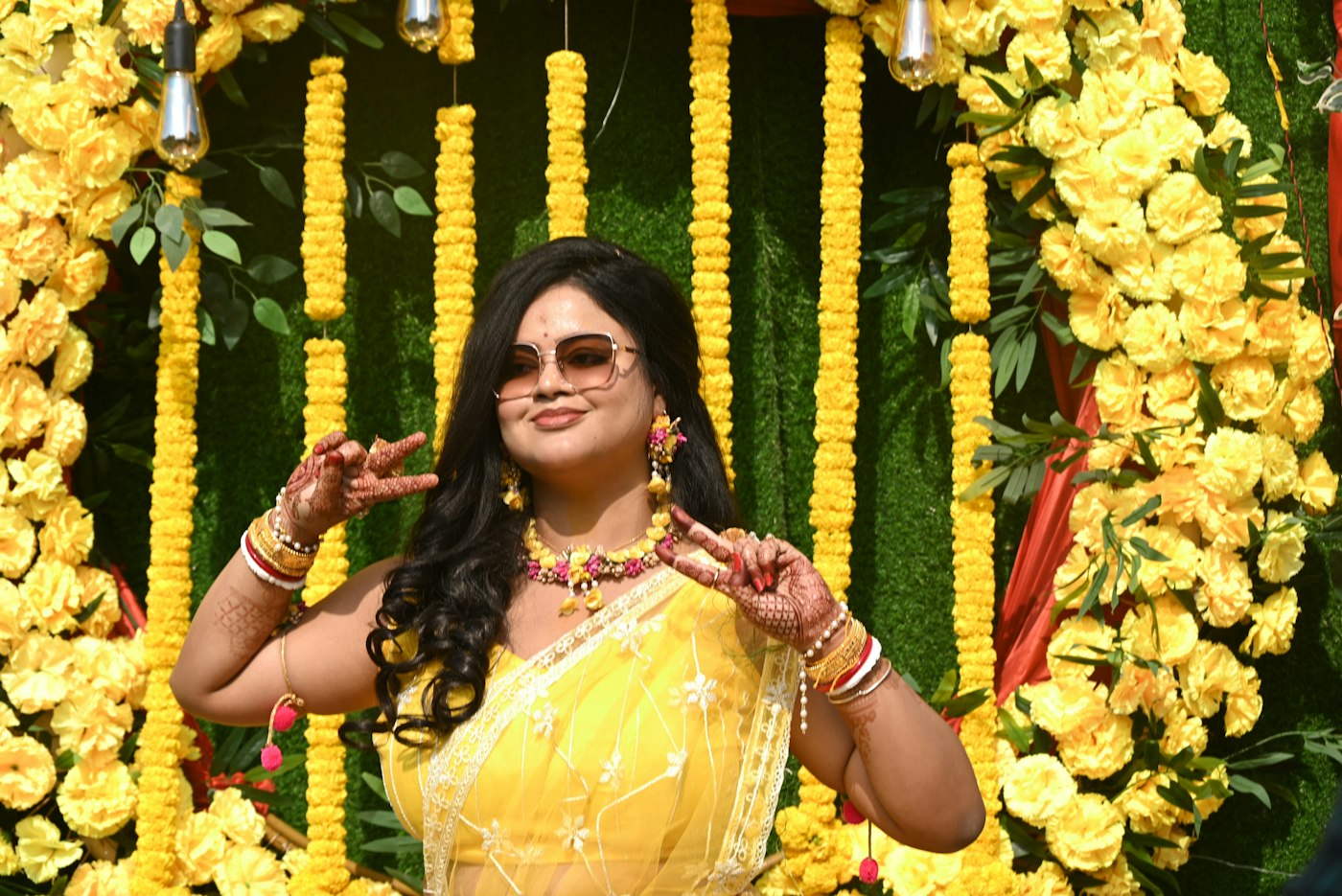 Guest in yellow at a haldi making a heart with her hands