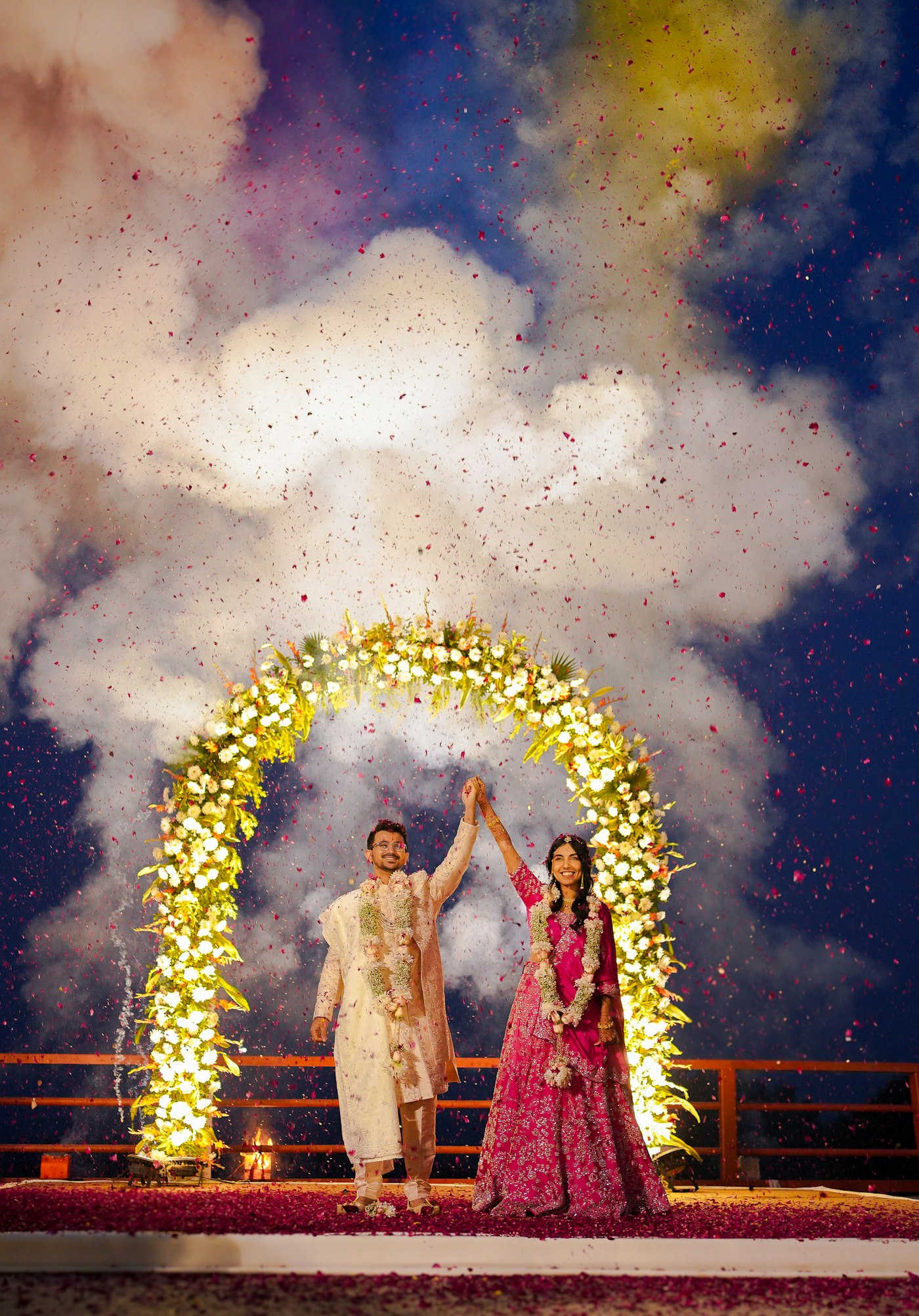 Varmala under a floral arch with confetti in the air